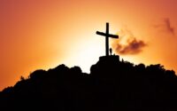 human standing beside crucifix statue on mountain
