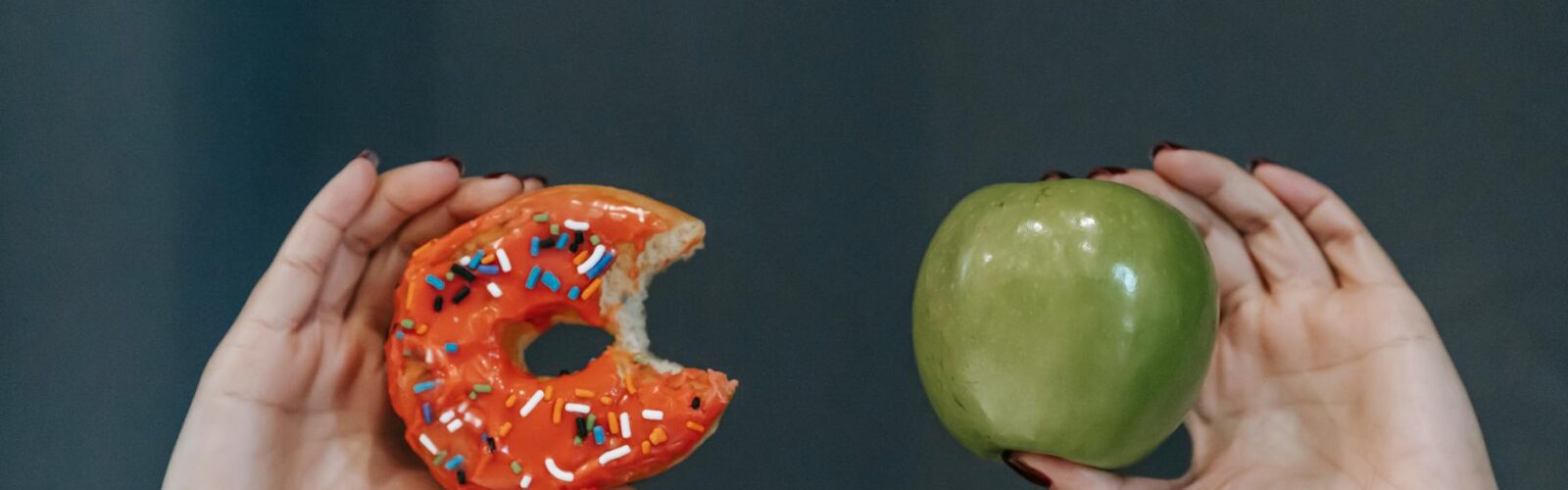 faceless woman showing fresh apple and sweet doughnut