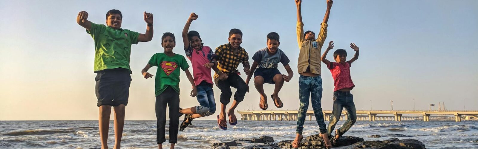 boy wearing green crew neck shirt jumping from black stone on seashore