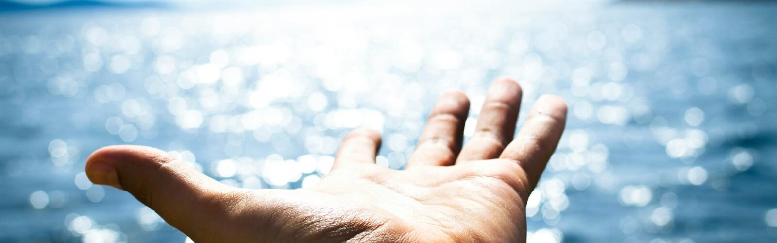 person hand reaching body of water
