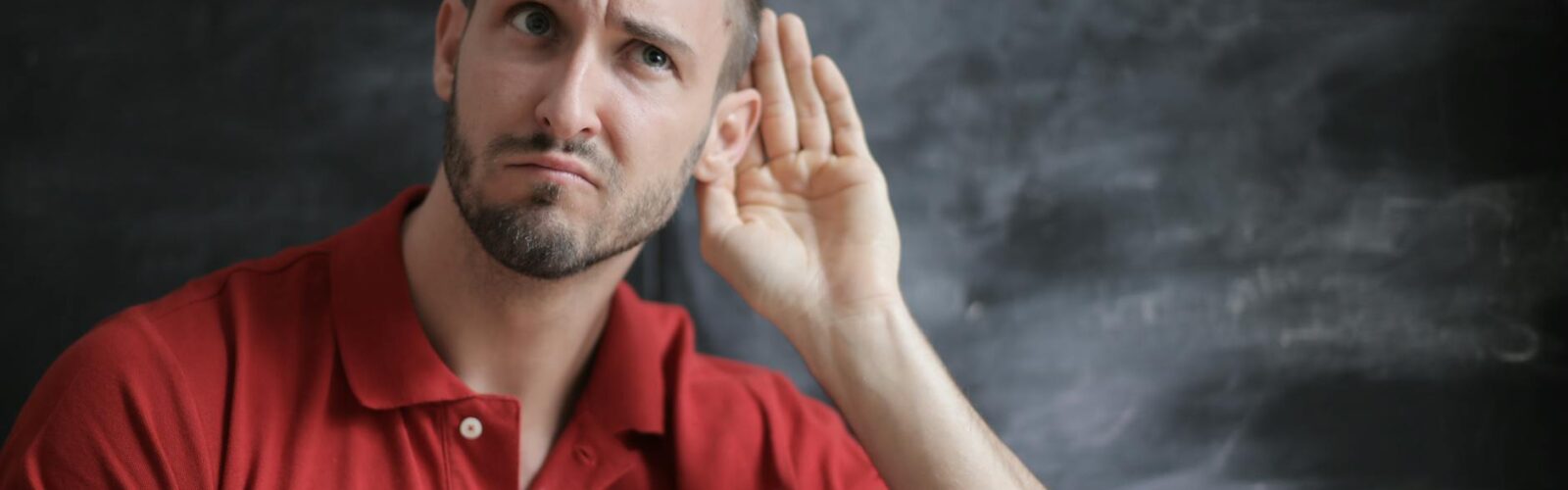 man in red polo shirt sitting near chalkboard