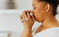 a close up shot of a woman holding a rosary while praying